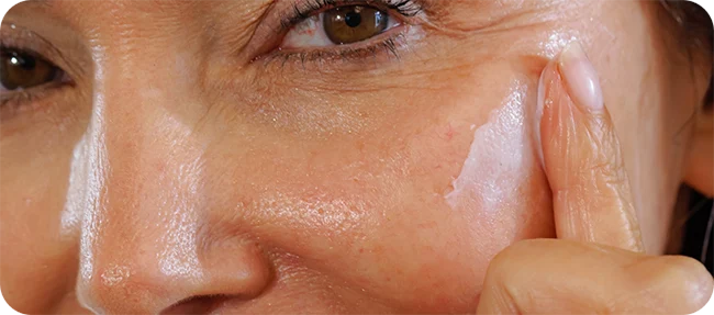 Close-up of a woman applying cream beside her eye