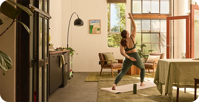 Woman stretching on a yoga mat in a sunlit living room